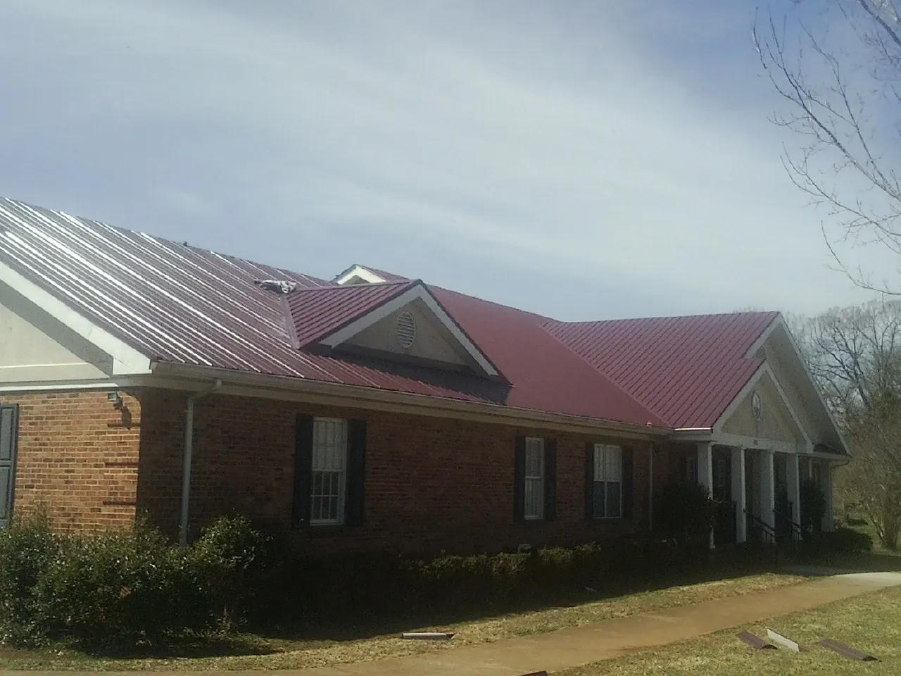 Red metal roof with gabled entries on a long brick building, from a Hail Damage Roof Repair job in Harmony