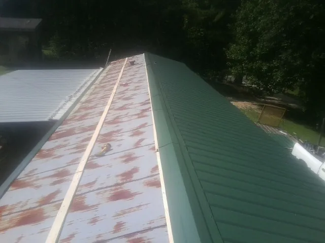 Old rusted panels beside newly installed green metal roofing — Wind Damage Roof Repair by Roofing Brothers in Harmony