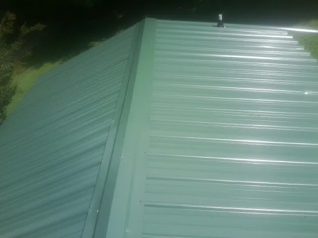 New green metal panels meeting at the ridge of a roof — Flat Roof Repair work by our crew in Harmony
