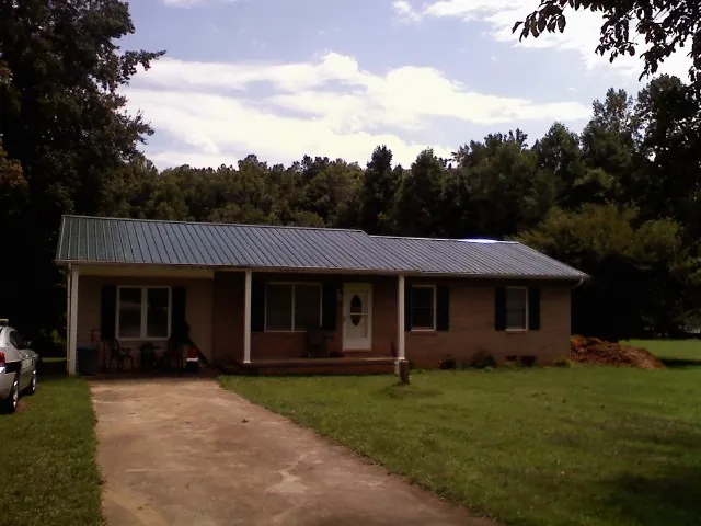 Dark green metal roof on a brick ranch with a covered porch in Harmony